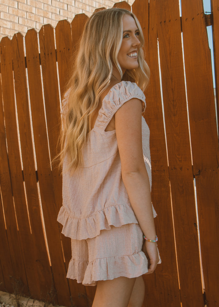 Woman in a light pink dress standing against a wooden fence