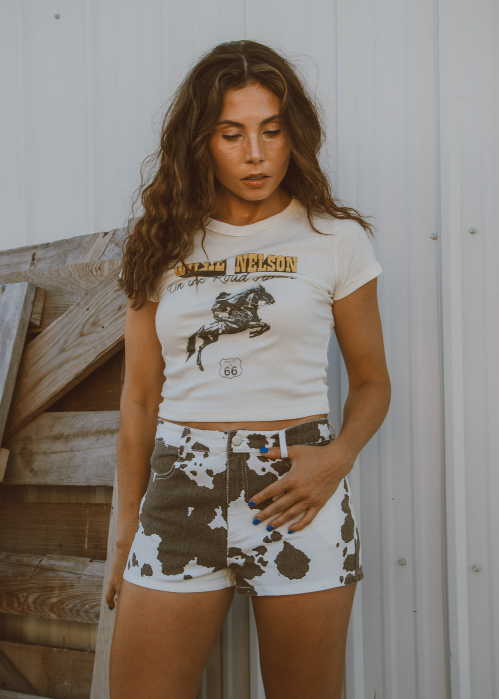 Woman wearing a white t-shirt with graphic design and patterned shorts against a wooden background