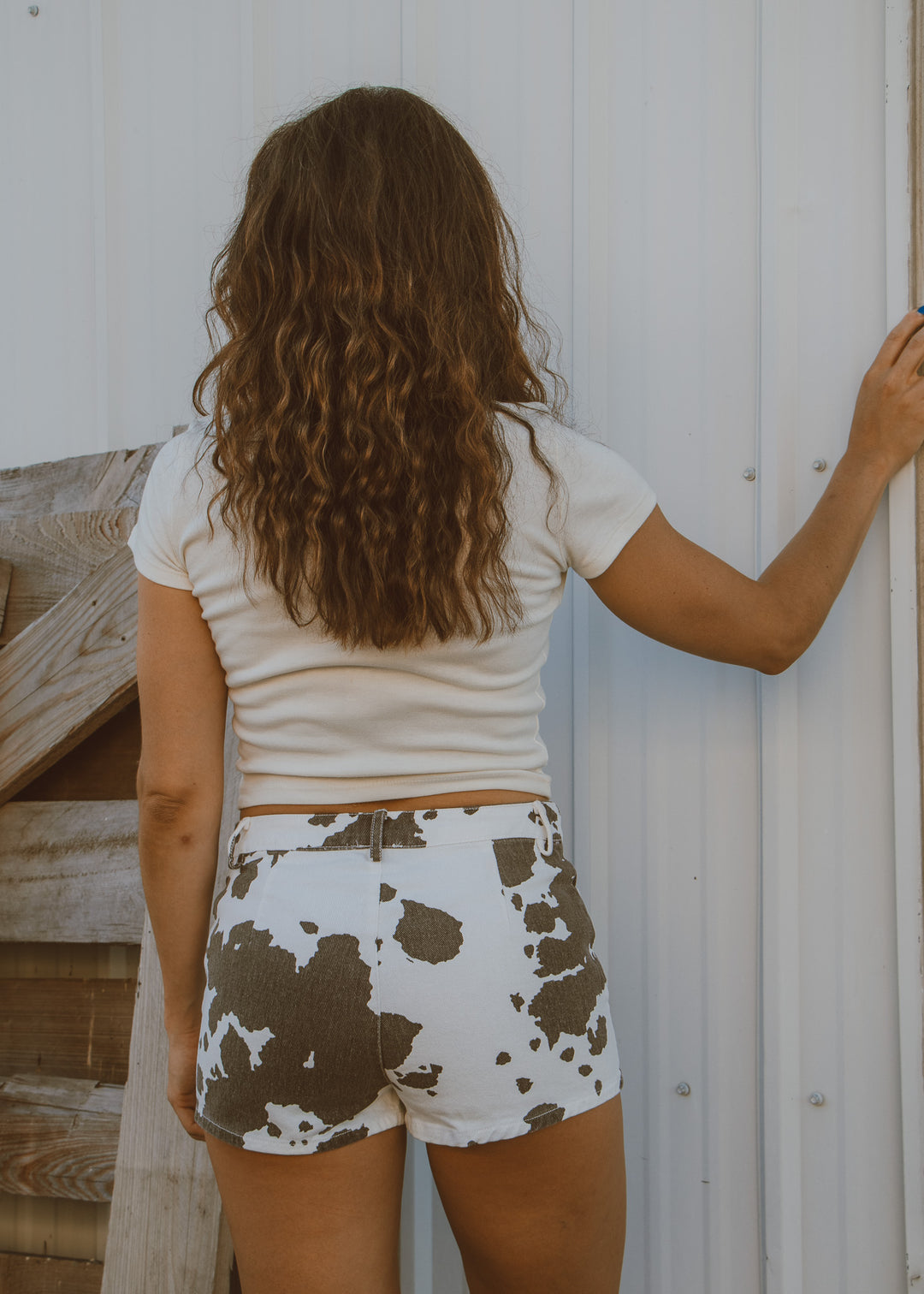 Person wearing a white shirt and cow print shorts standing against a white wall.