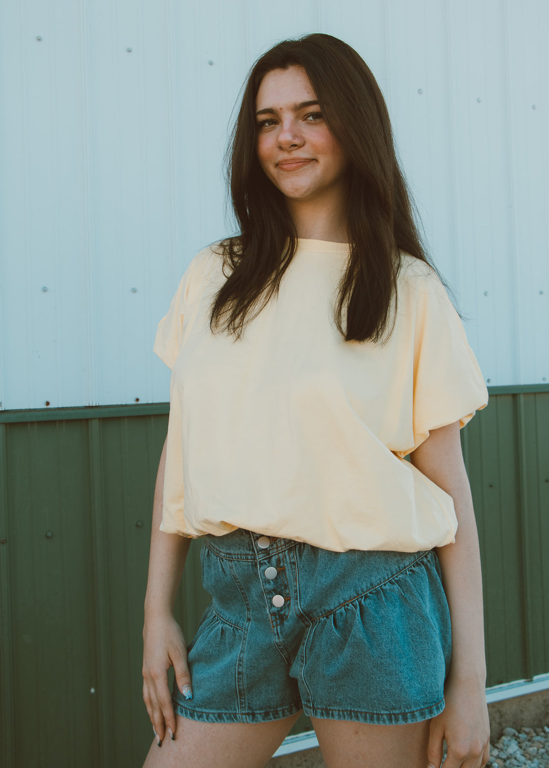 Woman wearing a light yellow top and denim shorts against a neutral background