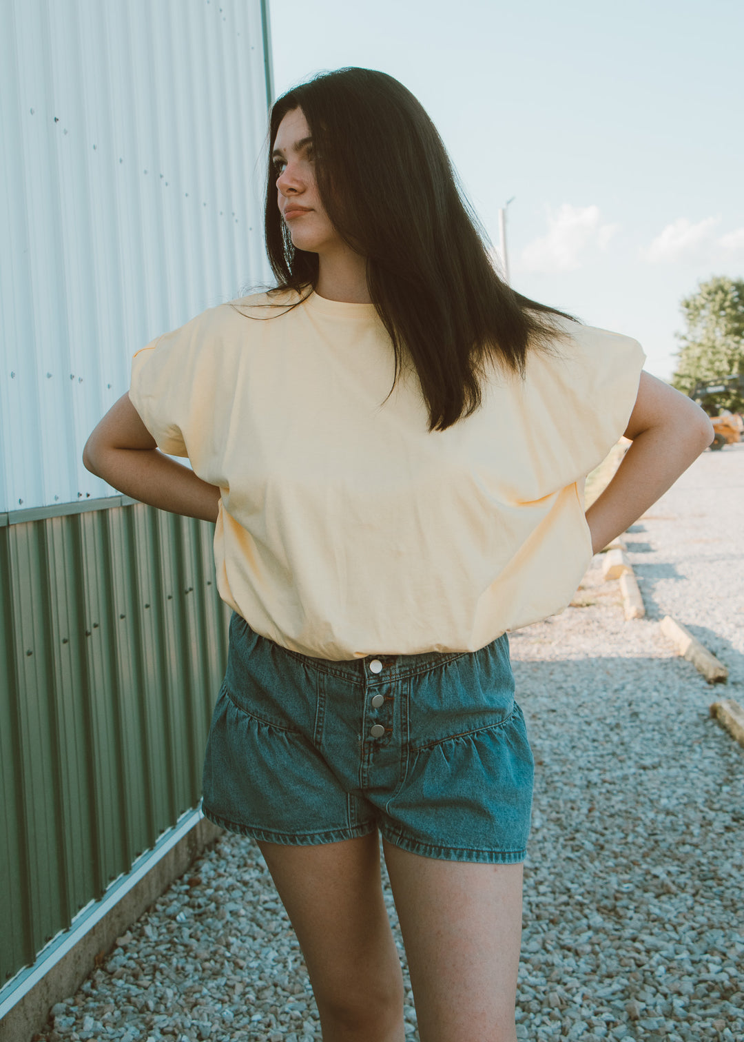 Woman wearing a yellow blouse and denim shorts standing outdoors.