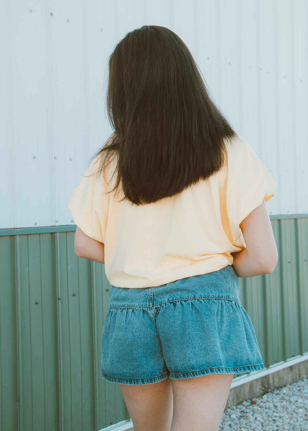 Person wearing a yellow top and blue shorts standing against a light-colored wall.