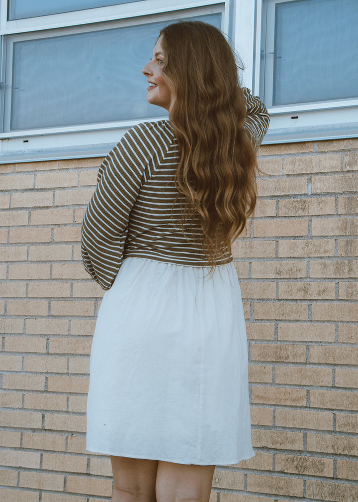 Woman wearing a striped sweater and white skirt standing against a brick wall.