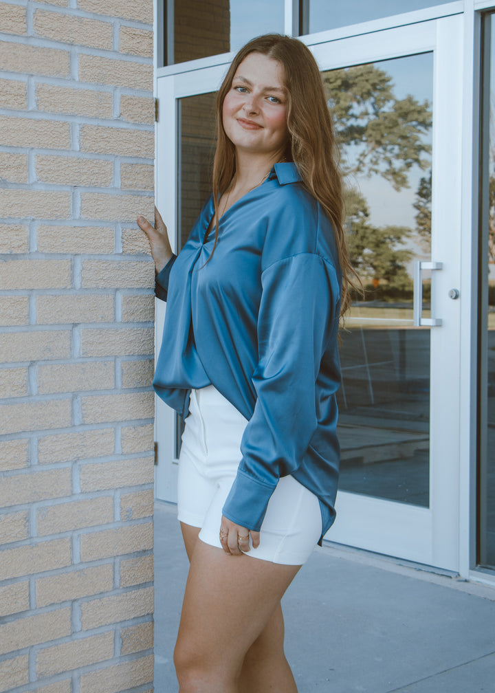 Woman in a blue shirt and white shorts standing next to a brick wall.
