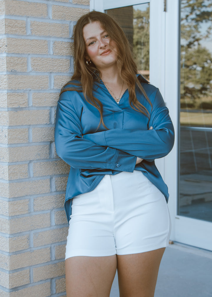 Woman wearing a blue satin blouse with white shorts.