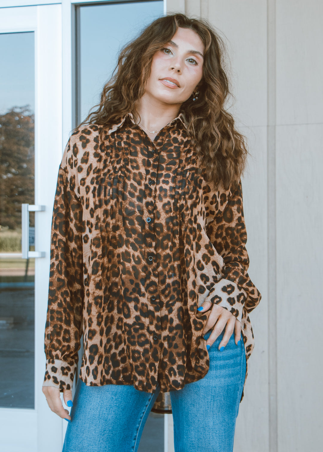 Woman wearing a leopard print shirt and blue jeans standing in front of a glass door.