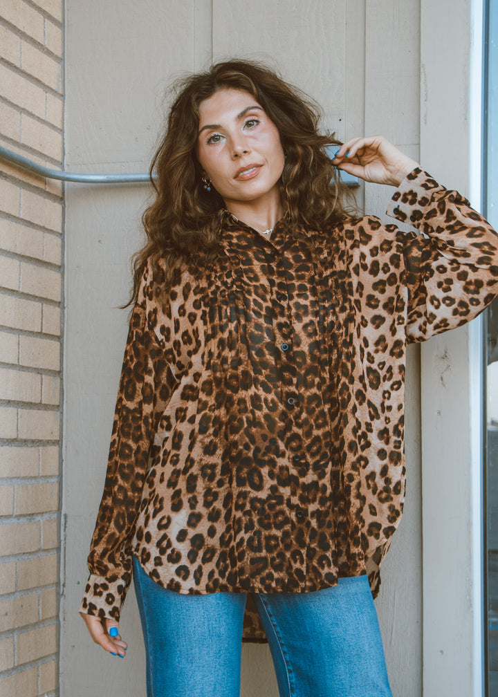 Woman wearing a leopard print shirt and blue jeans standing against a wall.