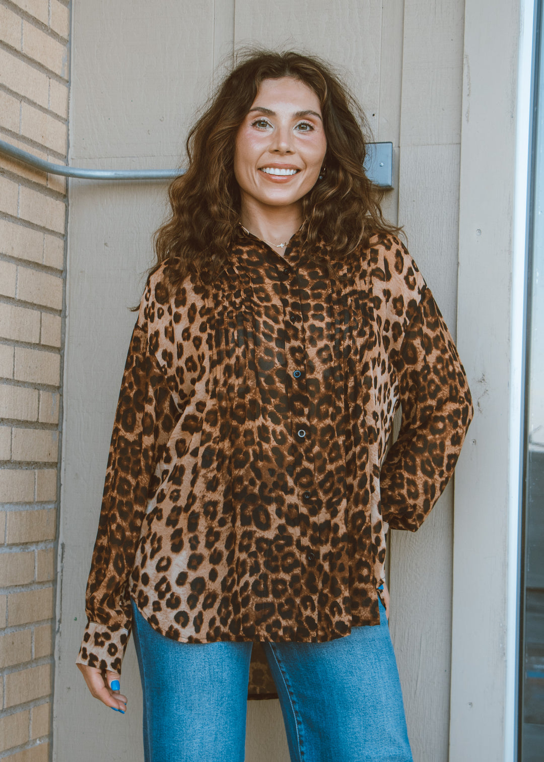 Woman wearing a leopard print shirt and blue jeans standing outside a building.