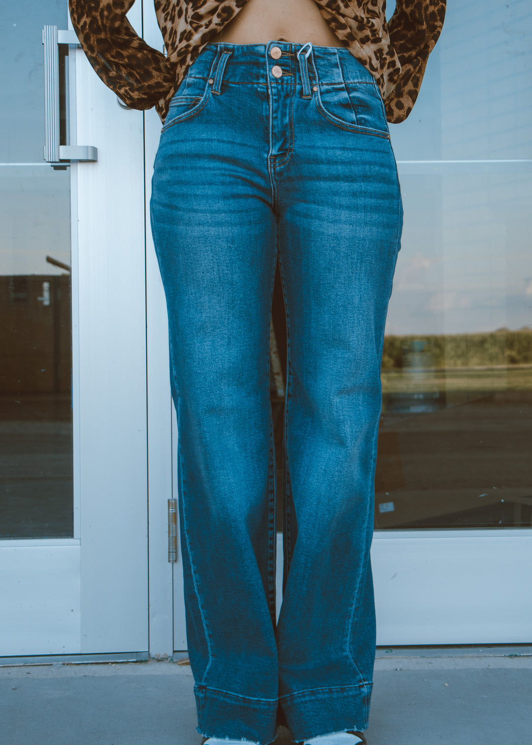 Person wearing blue jeans with a leopard print top in front of a glass door.