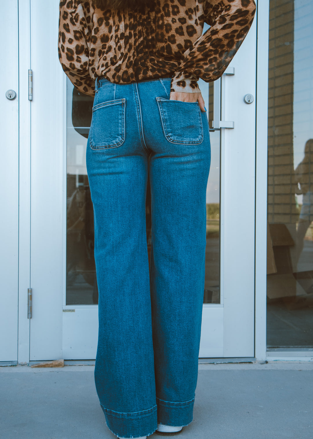 Person wearing a leopard print top and blue jeans standing in front of a glass door.