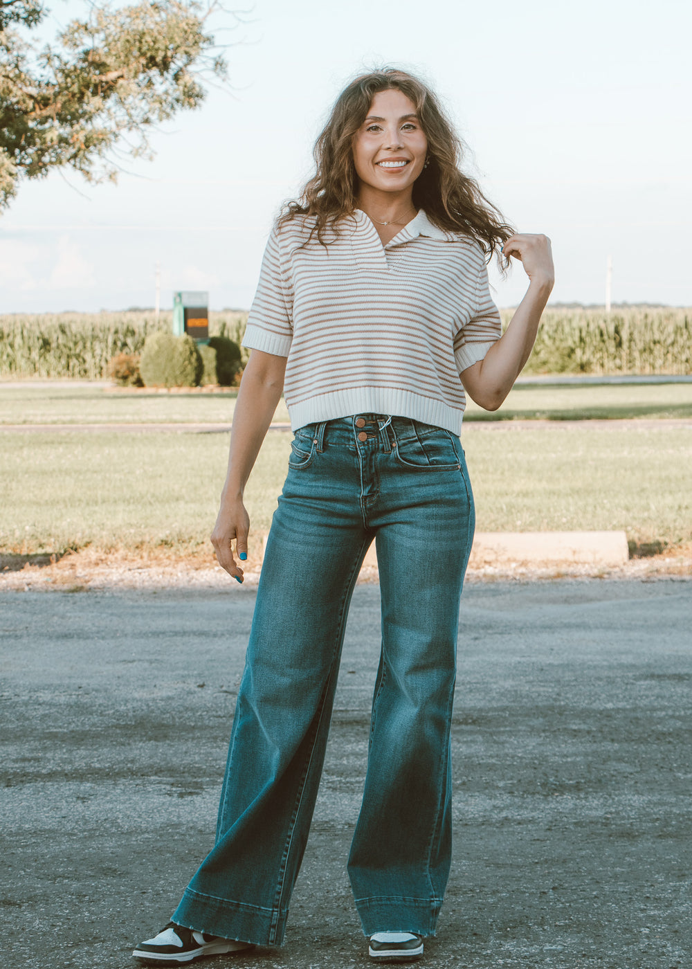 Woman wearing a striped shirt and blue jeans standing outdoors.