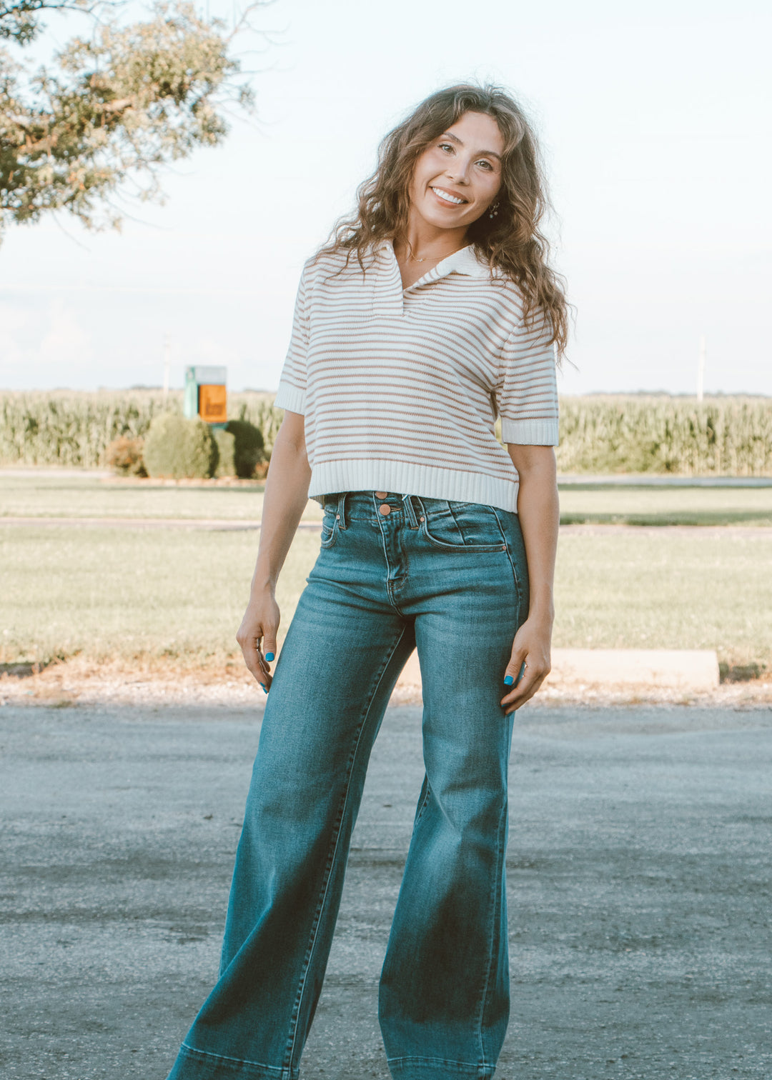 Woman wearing a striped shirt and blue jeans standing outdoors.