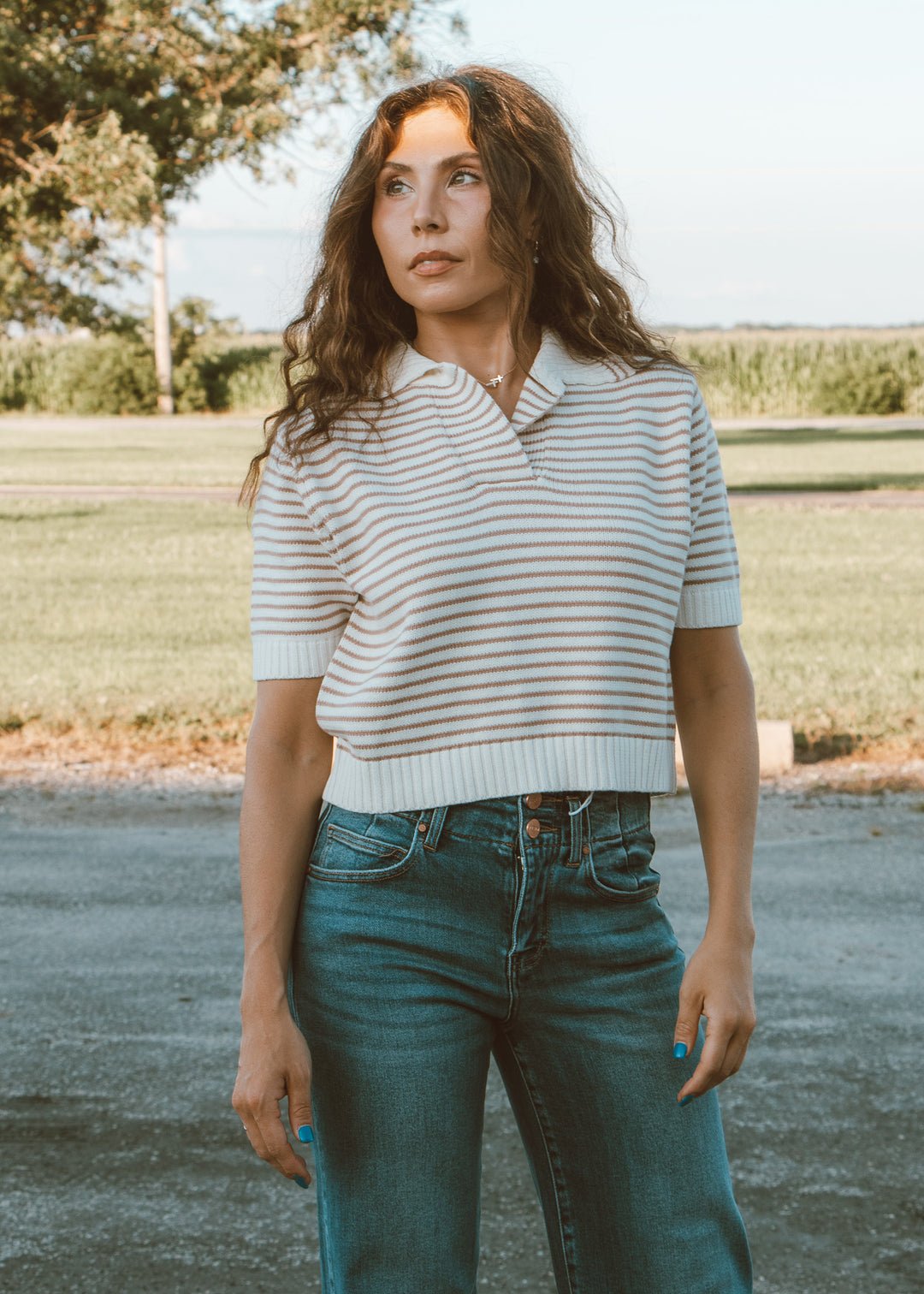 Woman wearing a striped shirt and jeans standing outdoors with a natural background