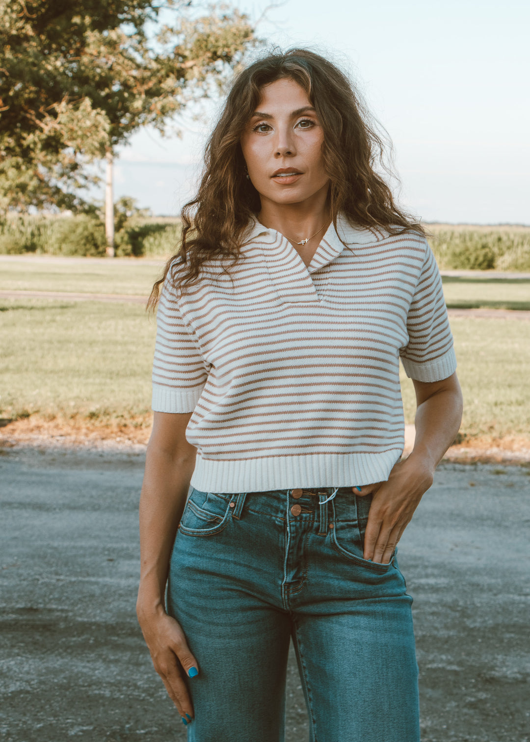 Woman wearing a striped shirt and jeans standing outdoors with a natural background