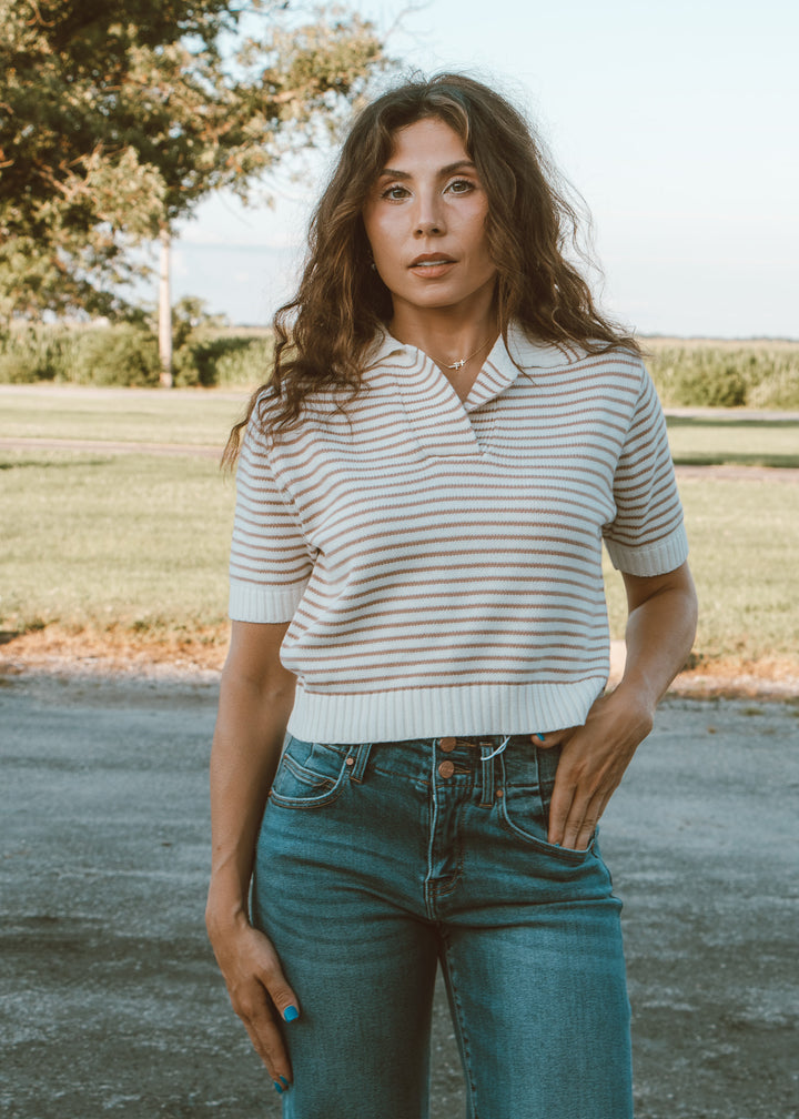 Woman wearing a striped shirt and jeans standing outdoors with a natural background