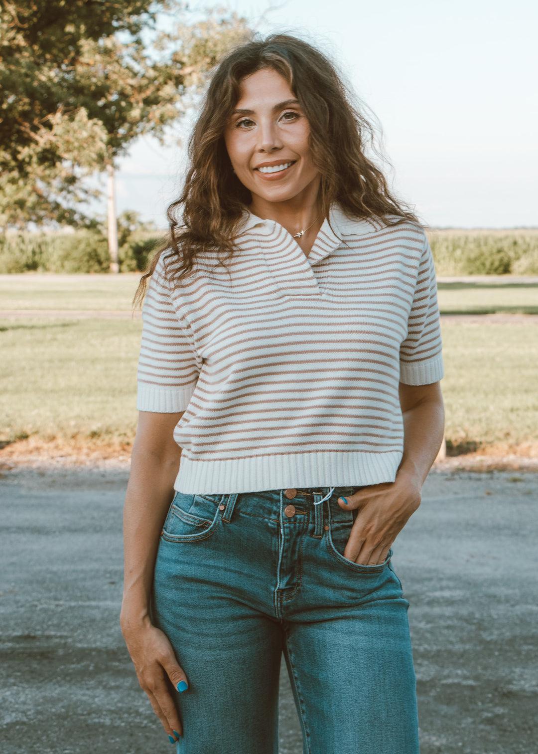 Woman wearing a striped shirt and jeans standing outdoors with trees in the background