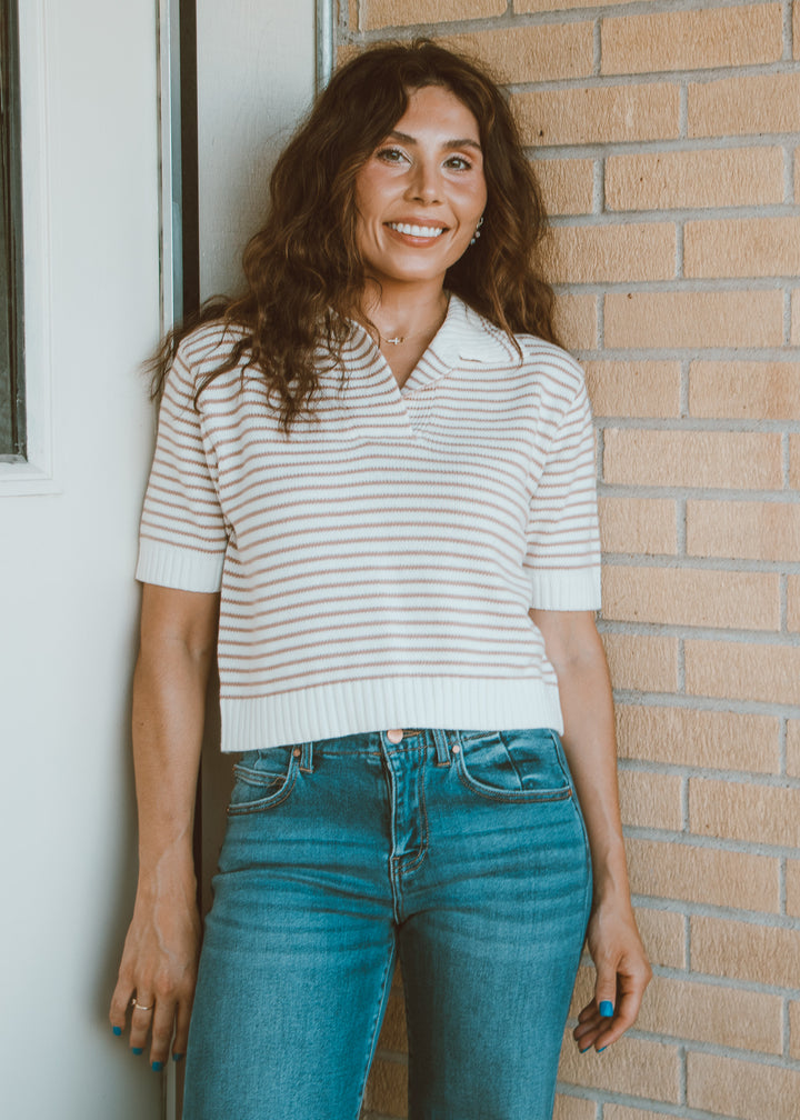 Woman wearing a striped shirt and jeans standing against a brick wall.