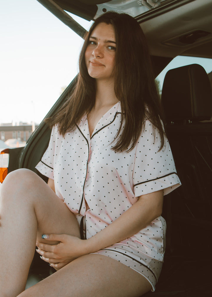 Woman in a pink polka dot outfit sitting in the back of a vehicle.