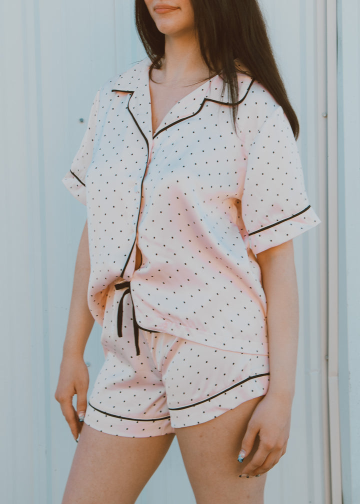 Woman wearing a polka dot pajama set against a light blue wall.