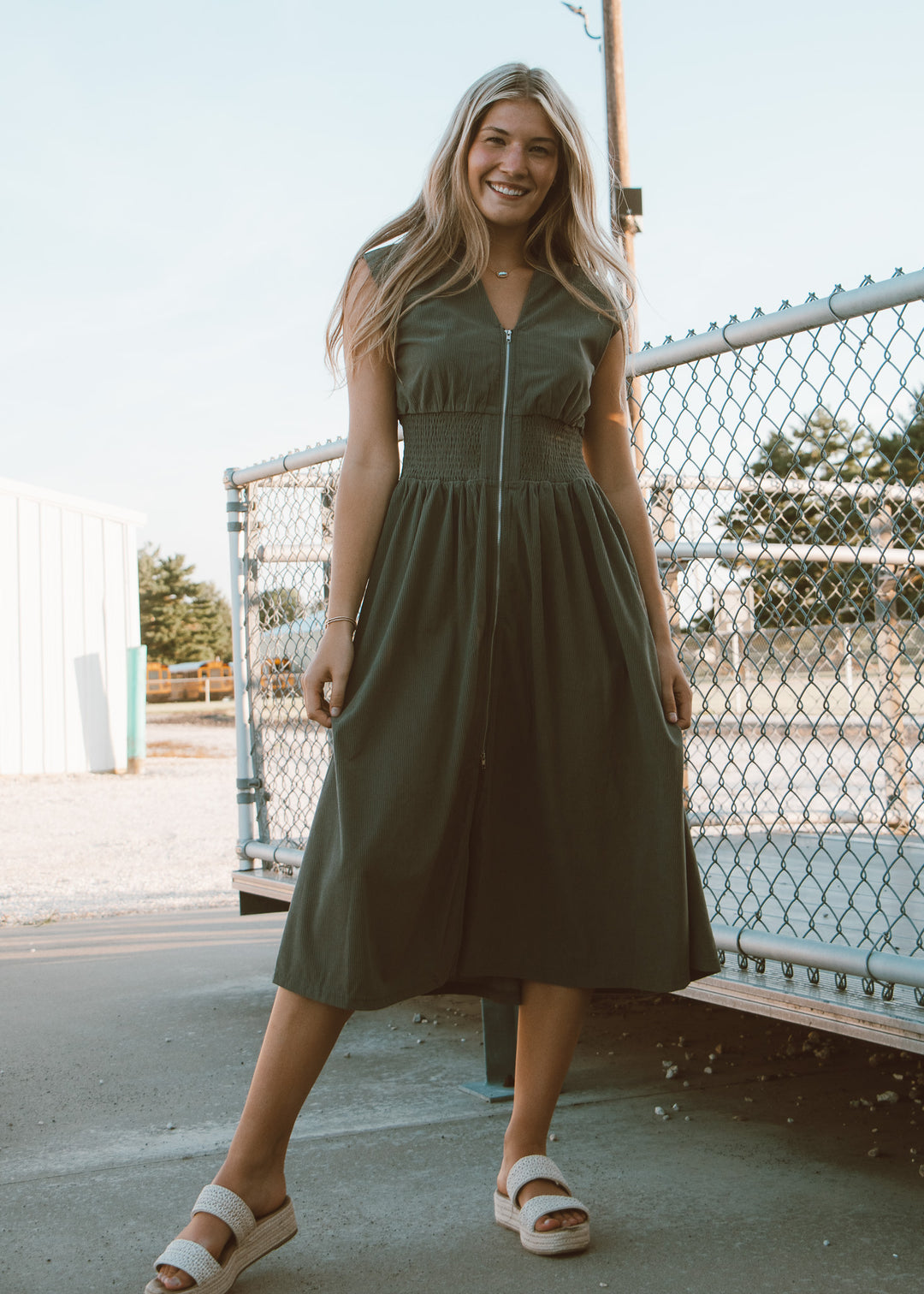Woman wearing a green dress standing outdoors near a fence.