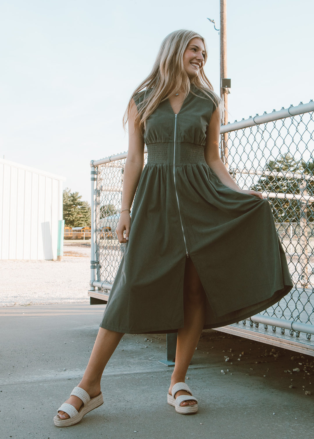 Woman wearing a green dress standing outdoors near a fence.