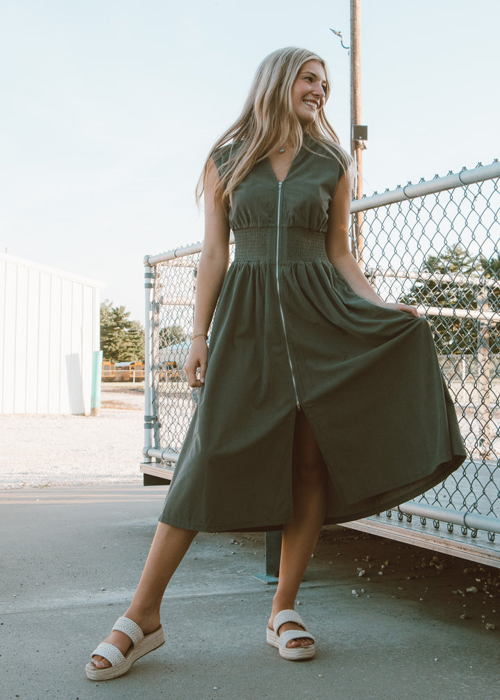 Woman wearing a green dress standing outdoors near a fence.
