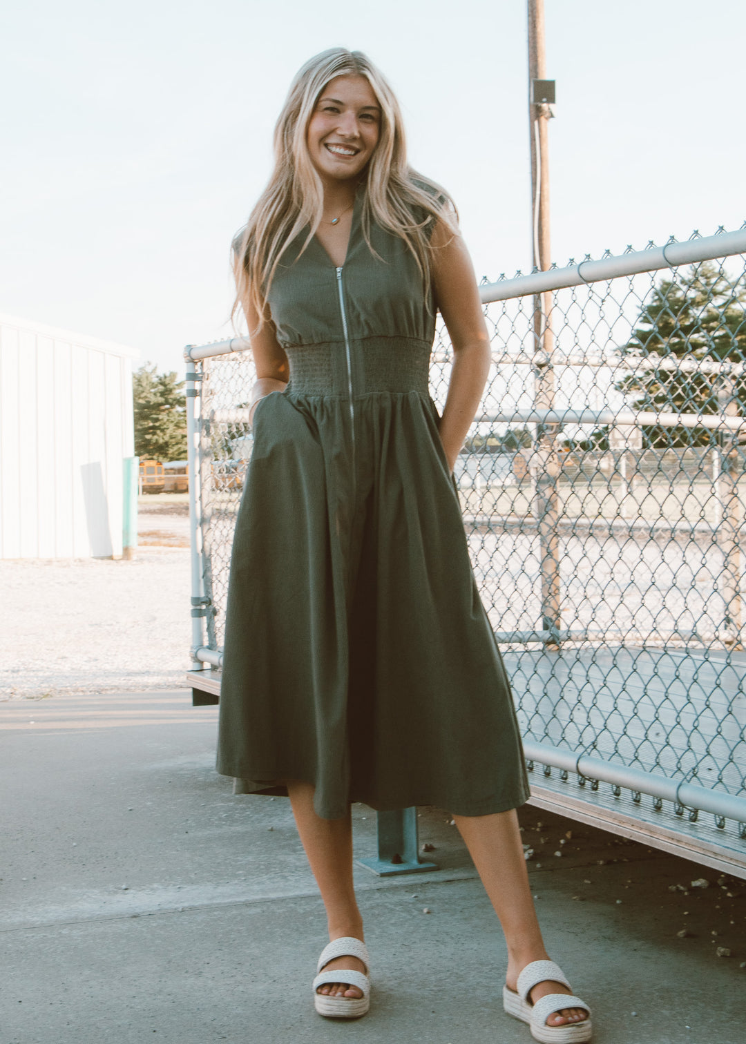 Woman wearing a green dress standing outdoors near a fence.