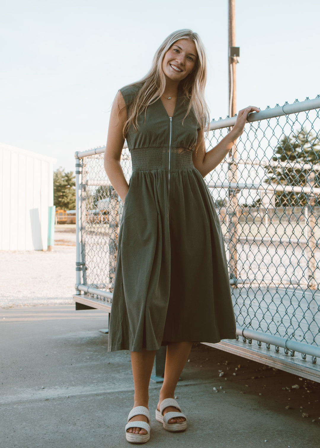 Woman in a green dress standing outdoors near a fence.