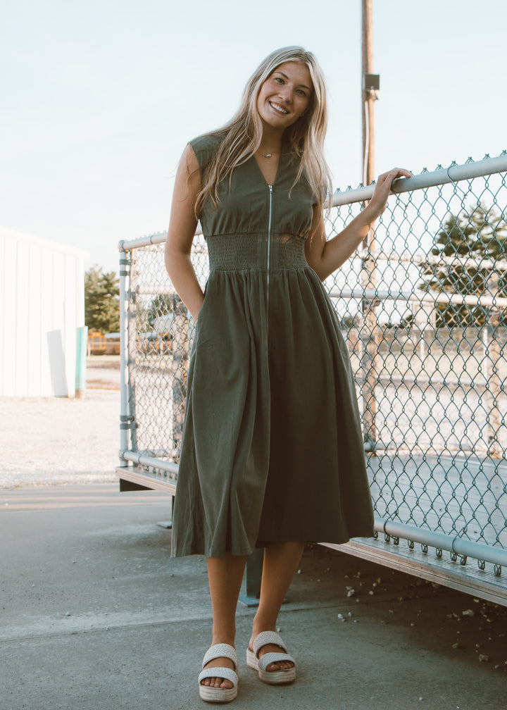 Woman in a green dress standing outdoors near a fence.