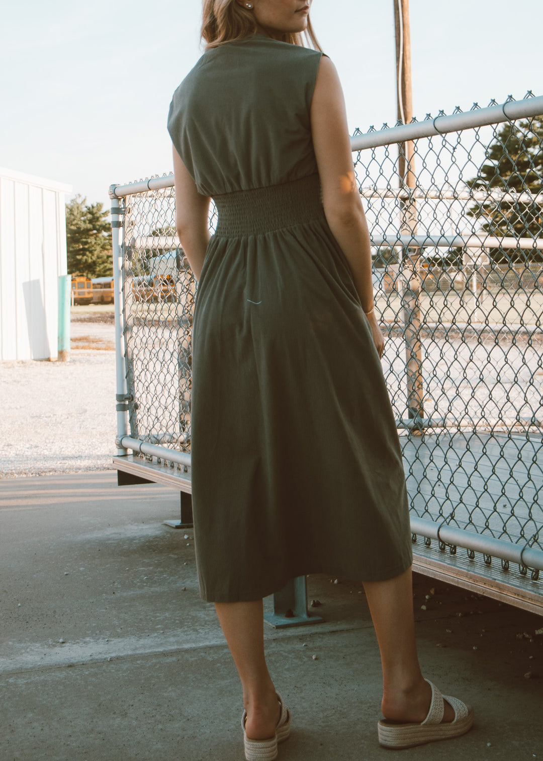 Woman wearing a green dress standing near a chain-link fence.