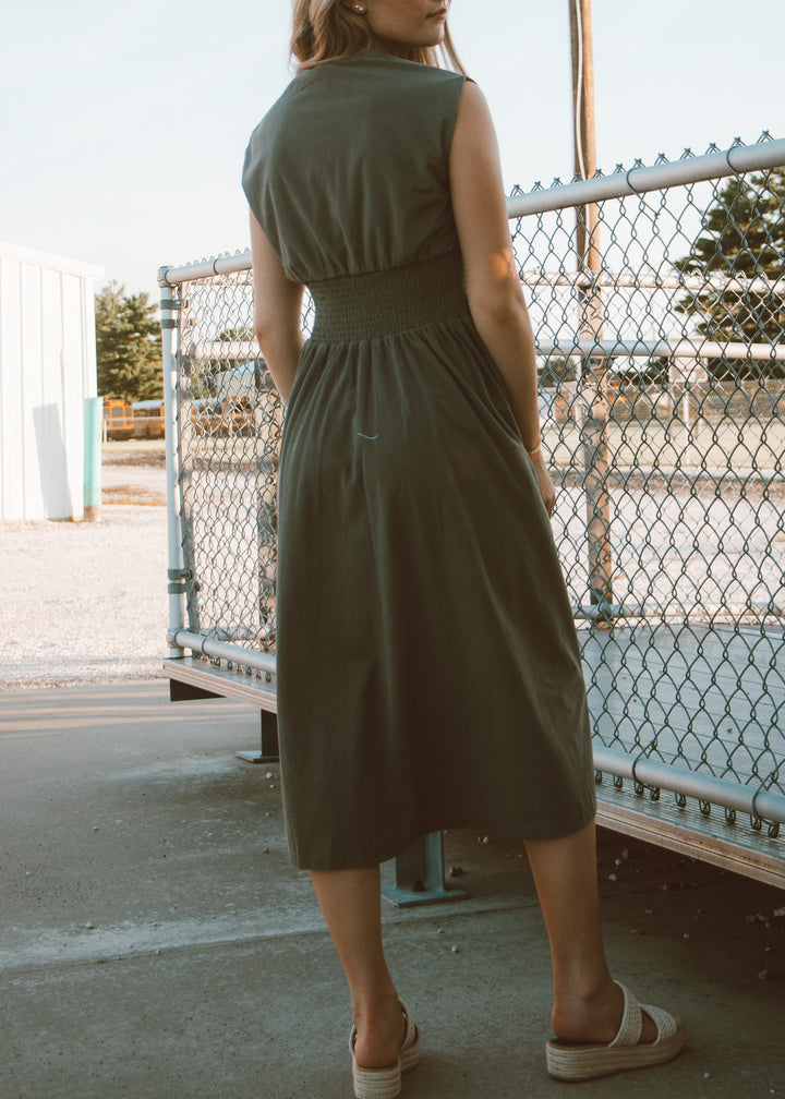 Woman wearing a green dress standing near a chain-link fence.