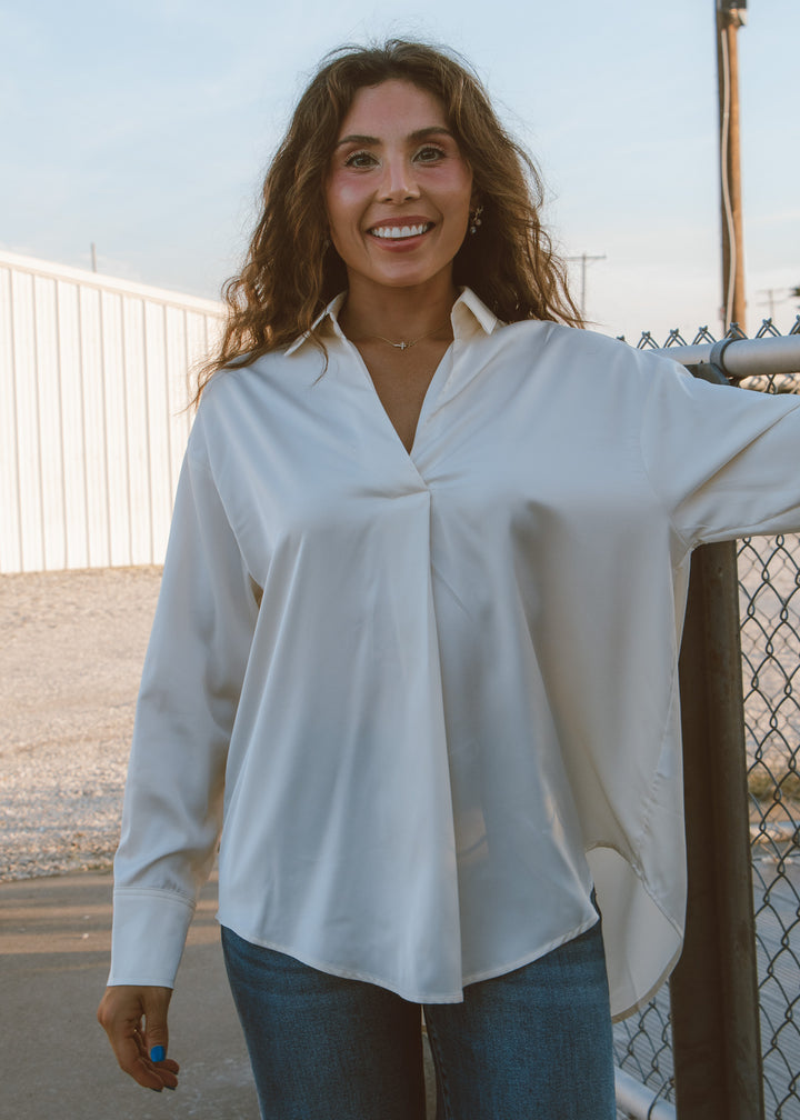 Woman wearing a white blouse and blue jeans standing outdoors.