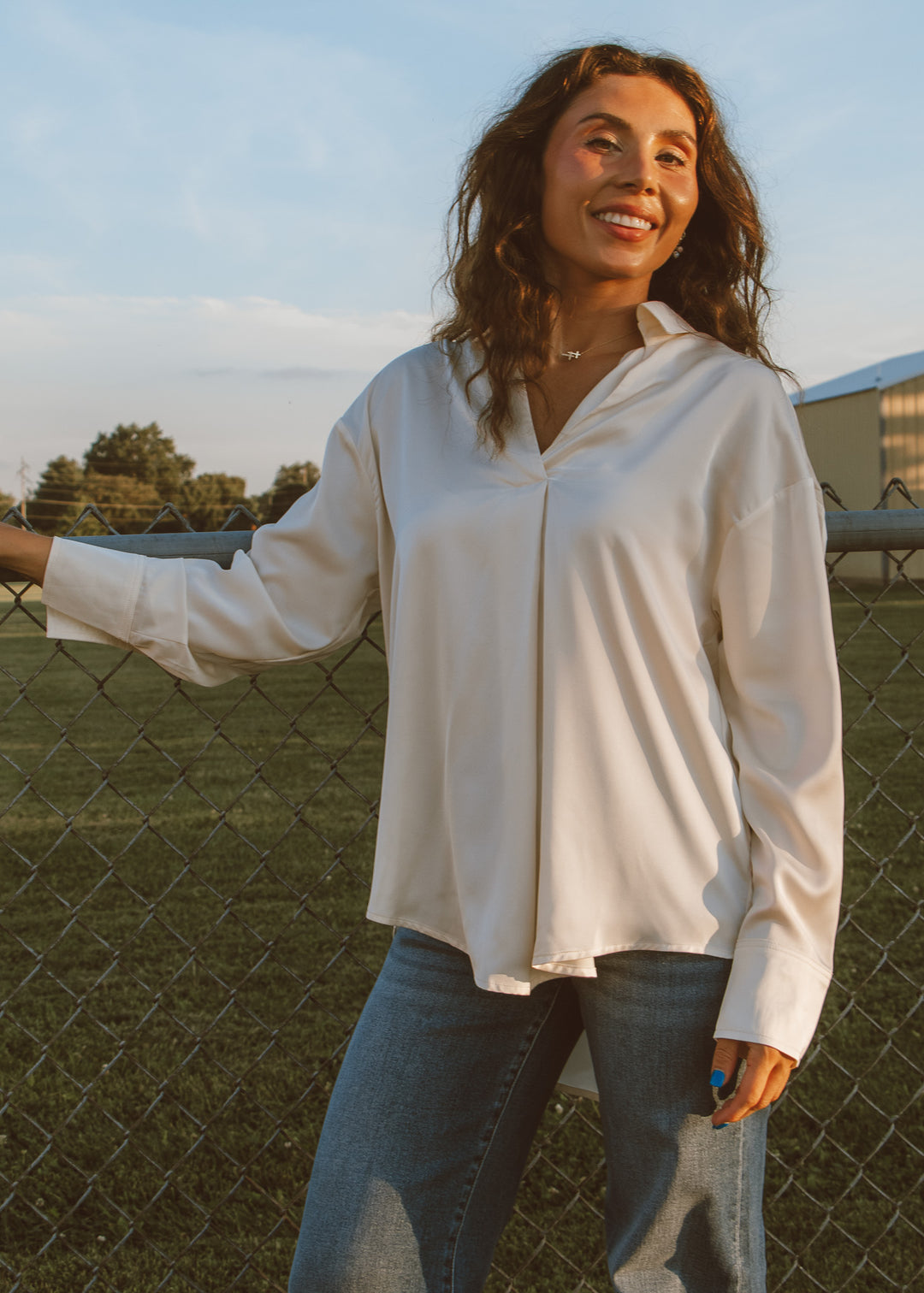 Woman wearing a white blouse and jeans standing by a fence with a scenic background