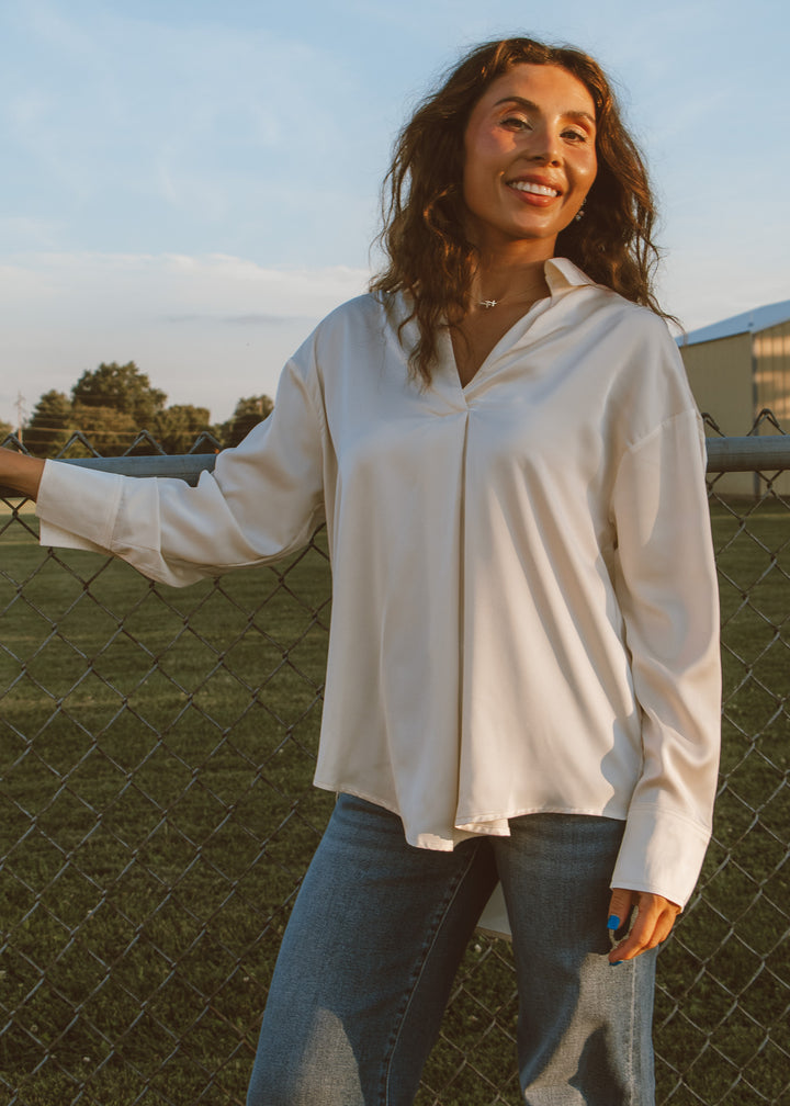 Woman wearing a white blouse and jeans standing by a fence with a scenic background