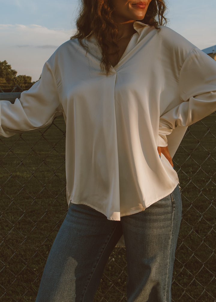 Person wearing a white shirt and jeans standing outdoors with a fence and trees in the background