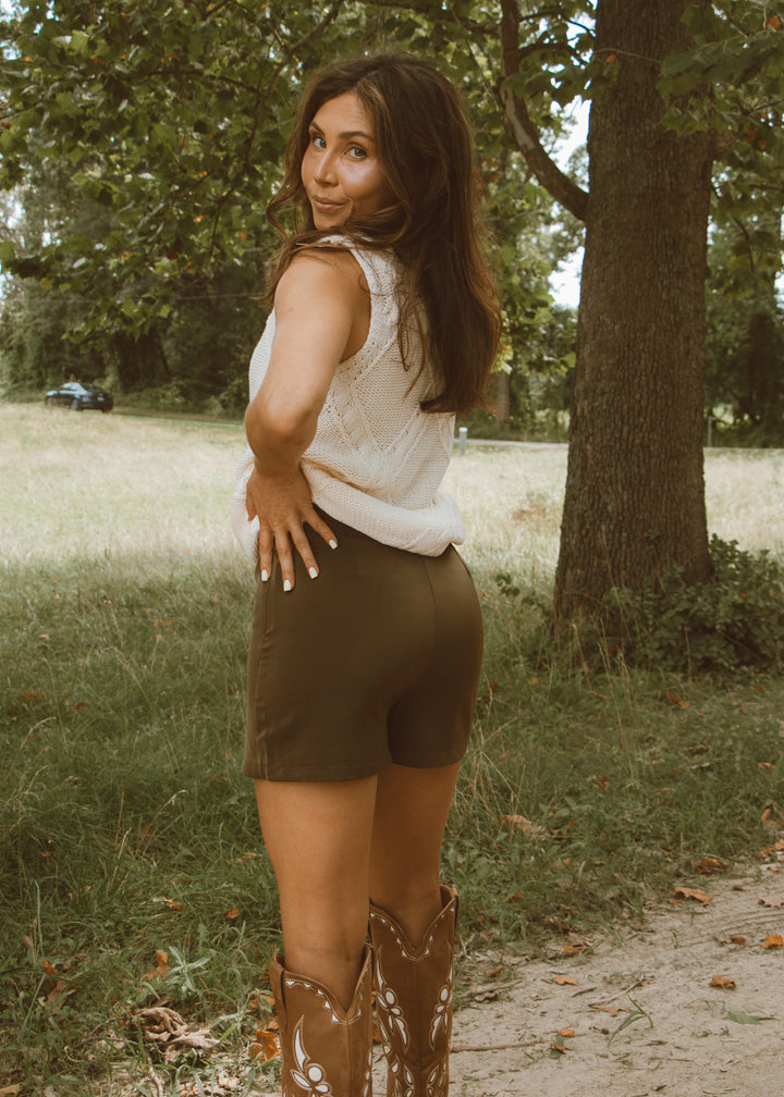 Woman standing outdoors in a natural setting with trees and grass.