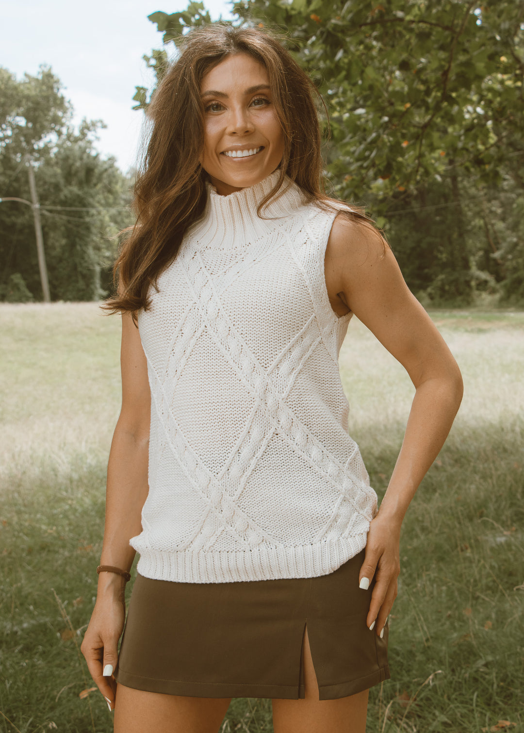 Woman wearing a white sleeveless knitted top in a natural setting