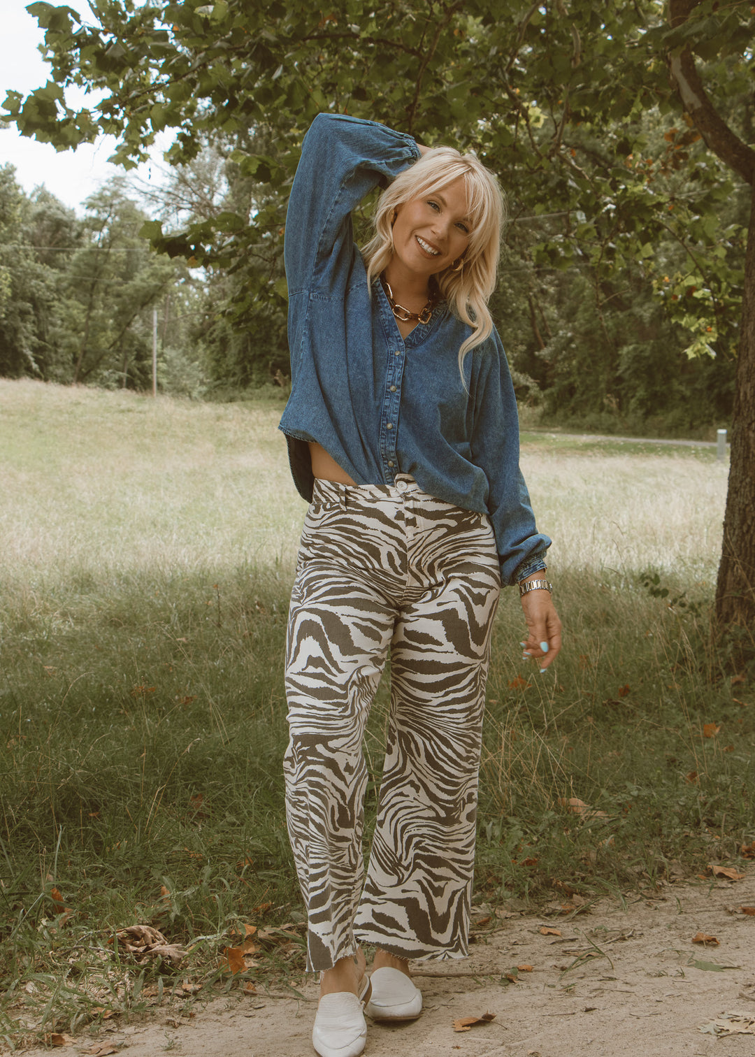 Woman in a blue shirt and zebra print pants standing outdoors in a natural setting