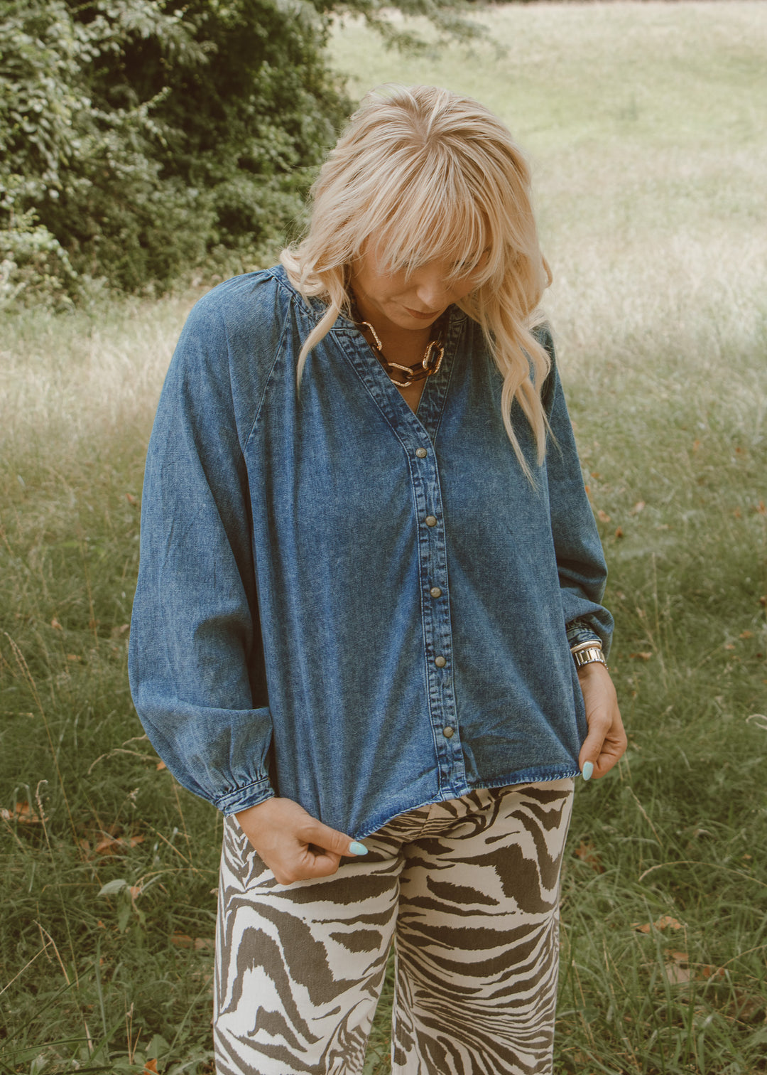 Person wearing a denim shirt and zebra print pants in a grassy field