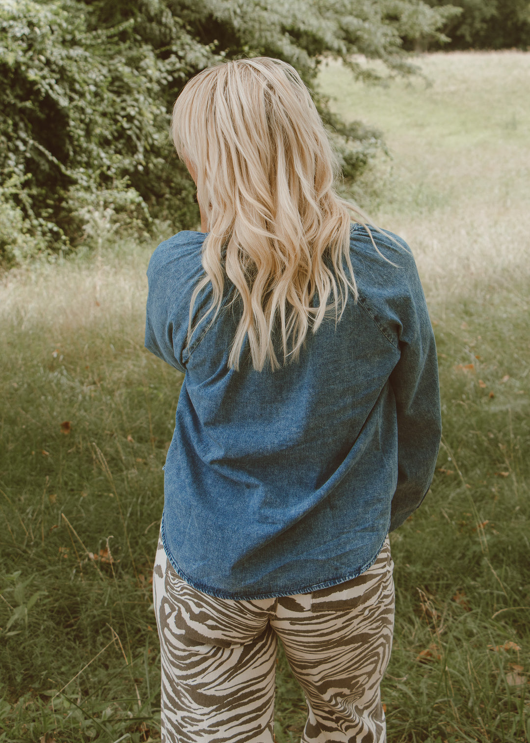 Person wearing a blue jacket and zebra print pants standing in a grassy field.