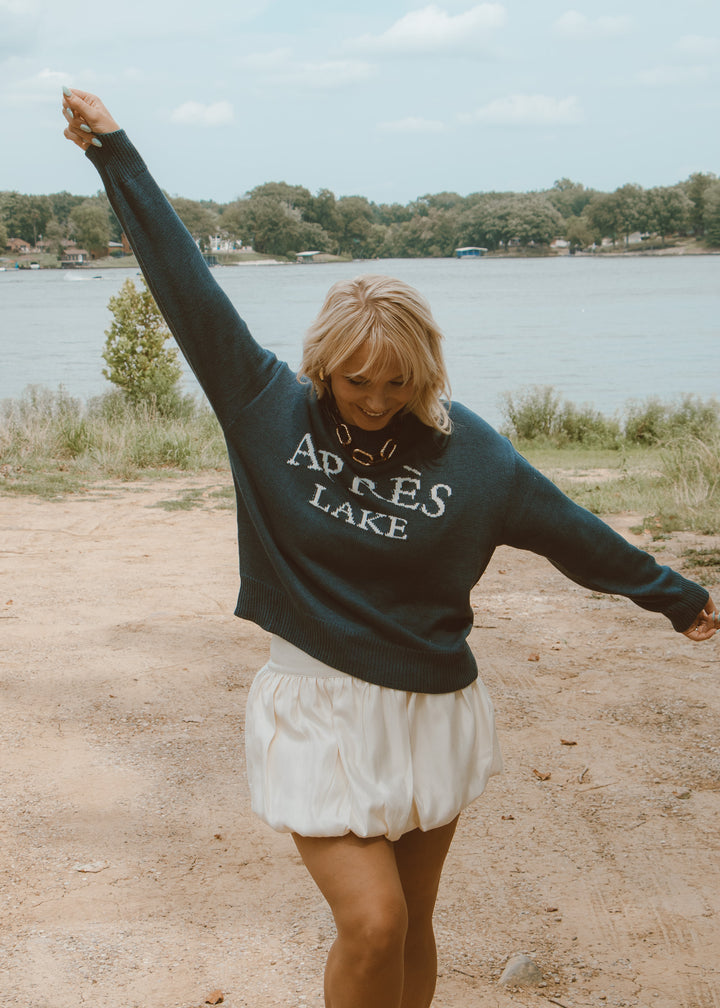 Woman in a sweatshirt with 'Apres Lake' text by a lake