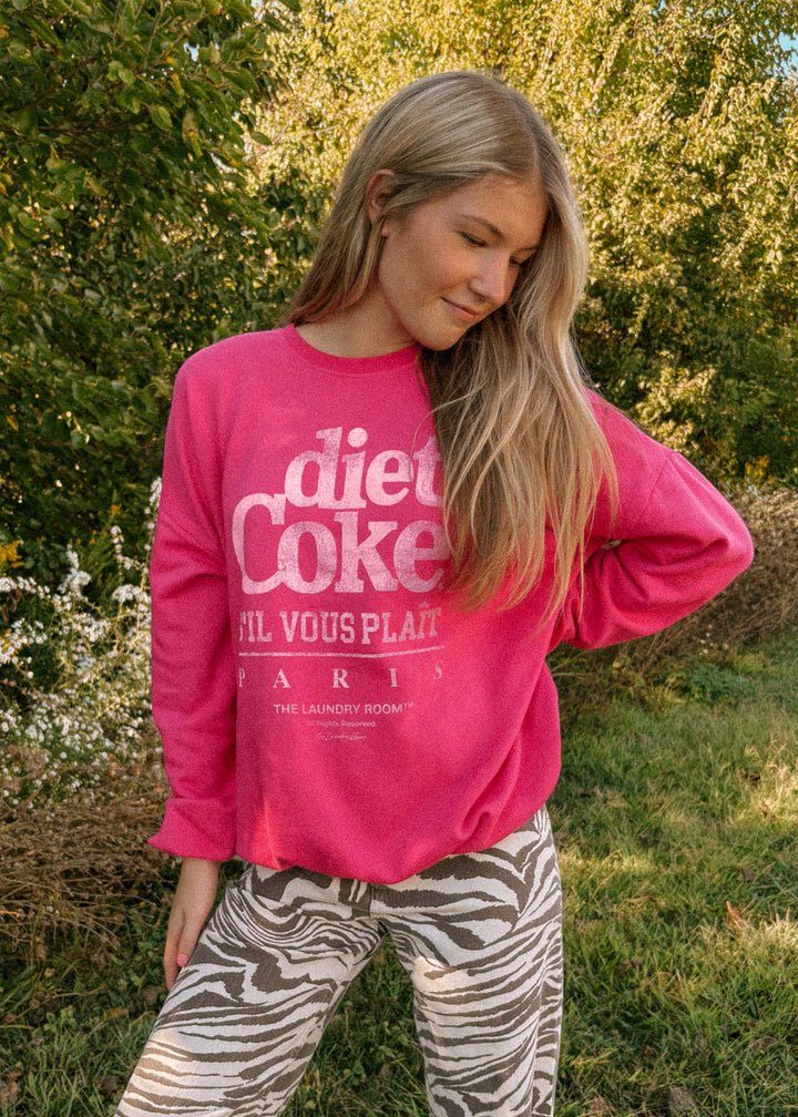 Person wearing a bright pink sweatshirt with text, standing outdoors in a natural setting.