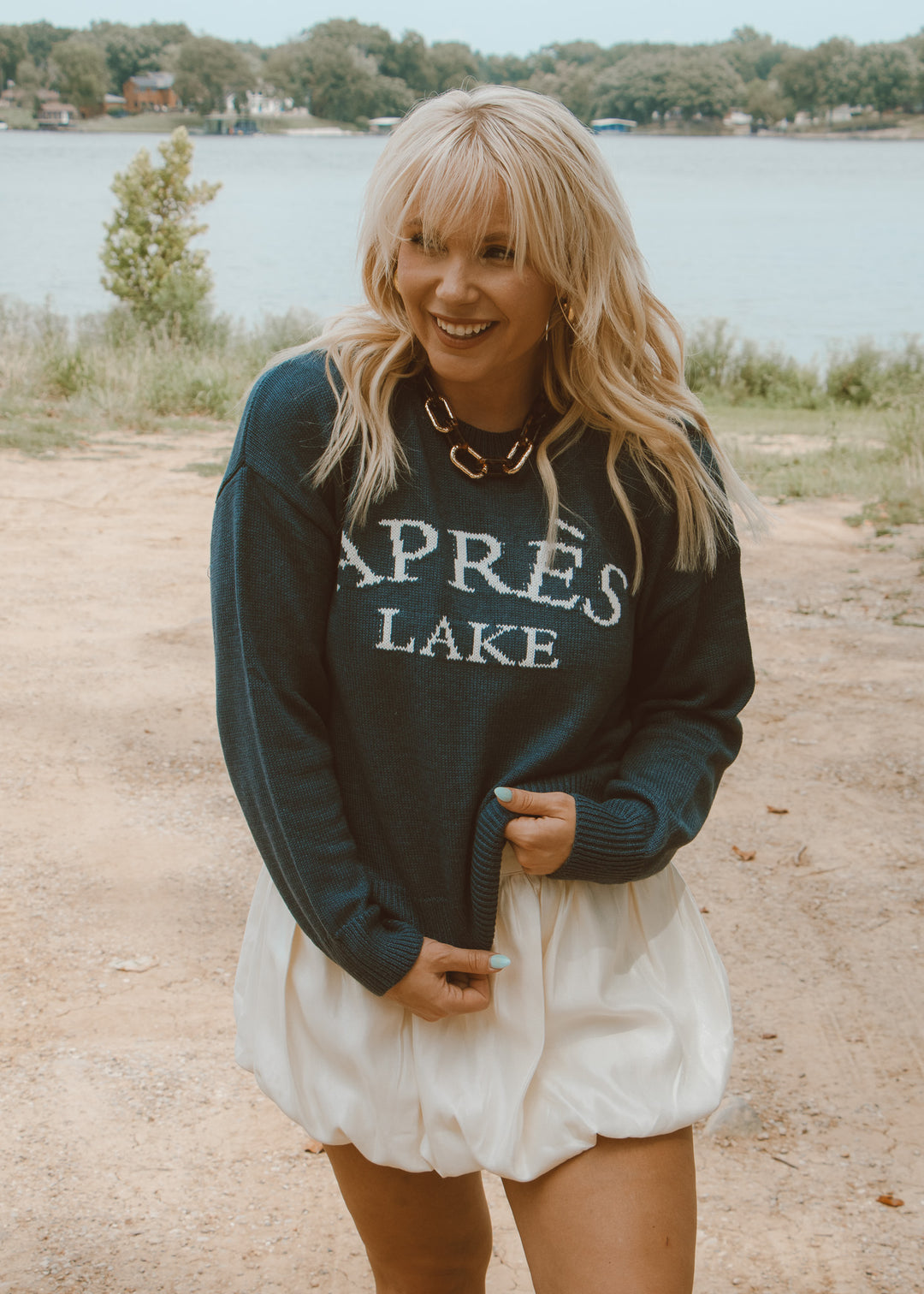 Woman wearing a sweatshirt with 'Après Lake' text by a lake.