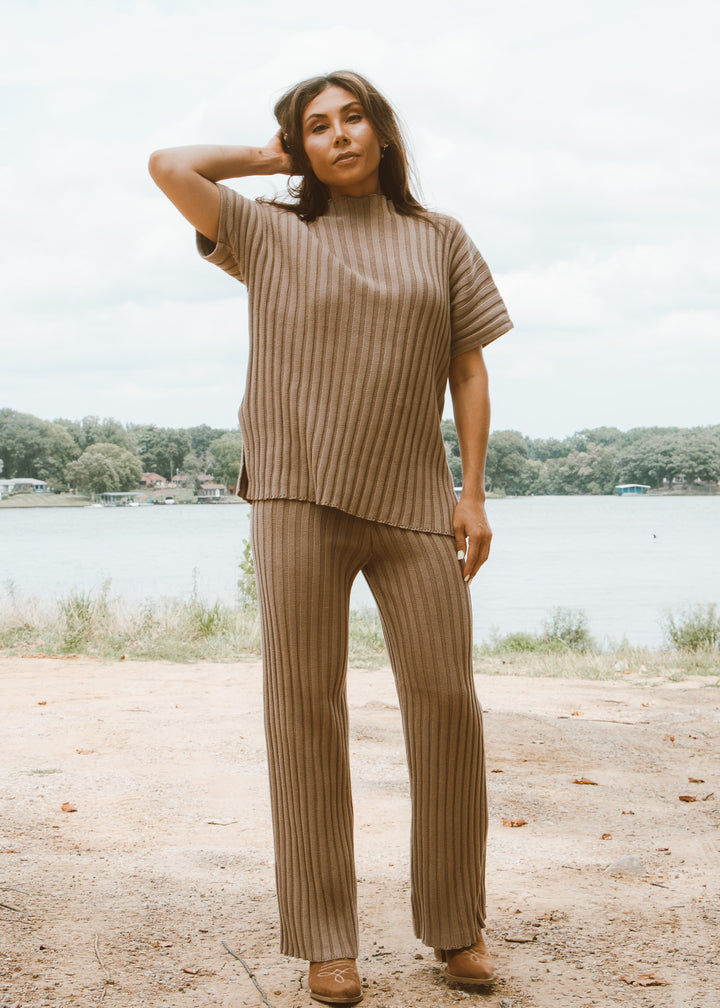 Woman wearing a matching ribbed sweater and pants set standing outdoors by a lake.