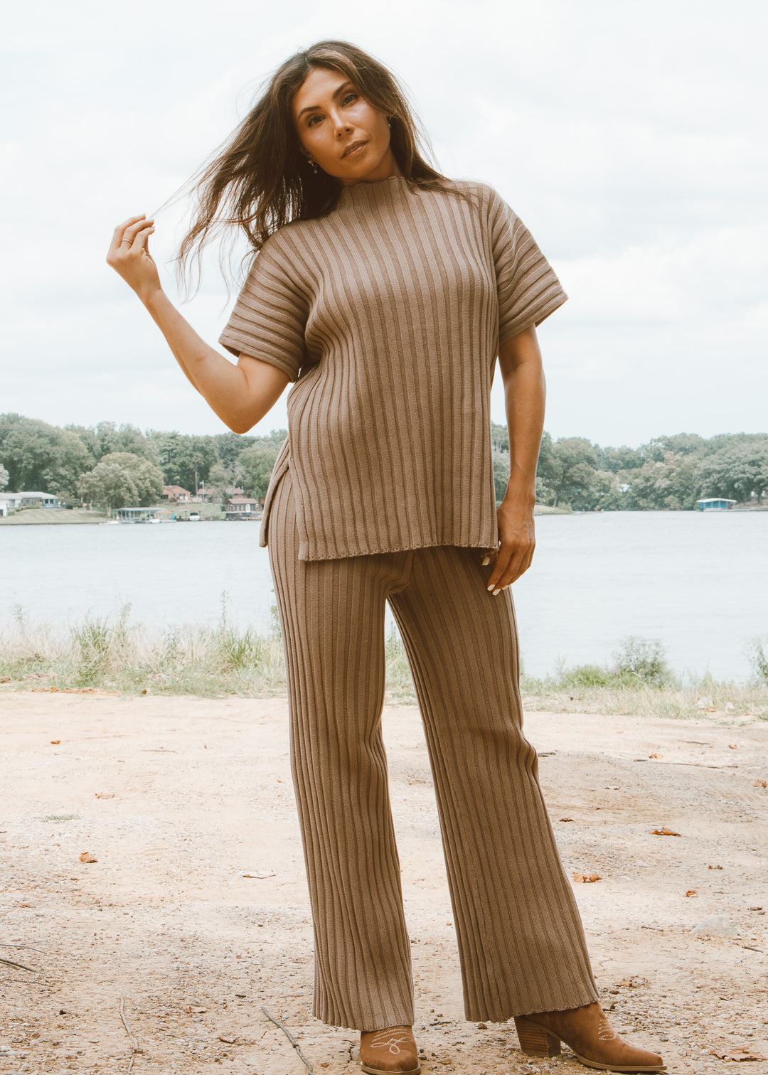 Woman wearing a brown ribbed outfit standing by a lake.
