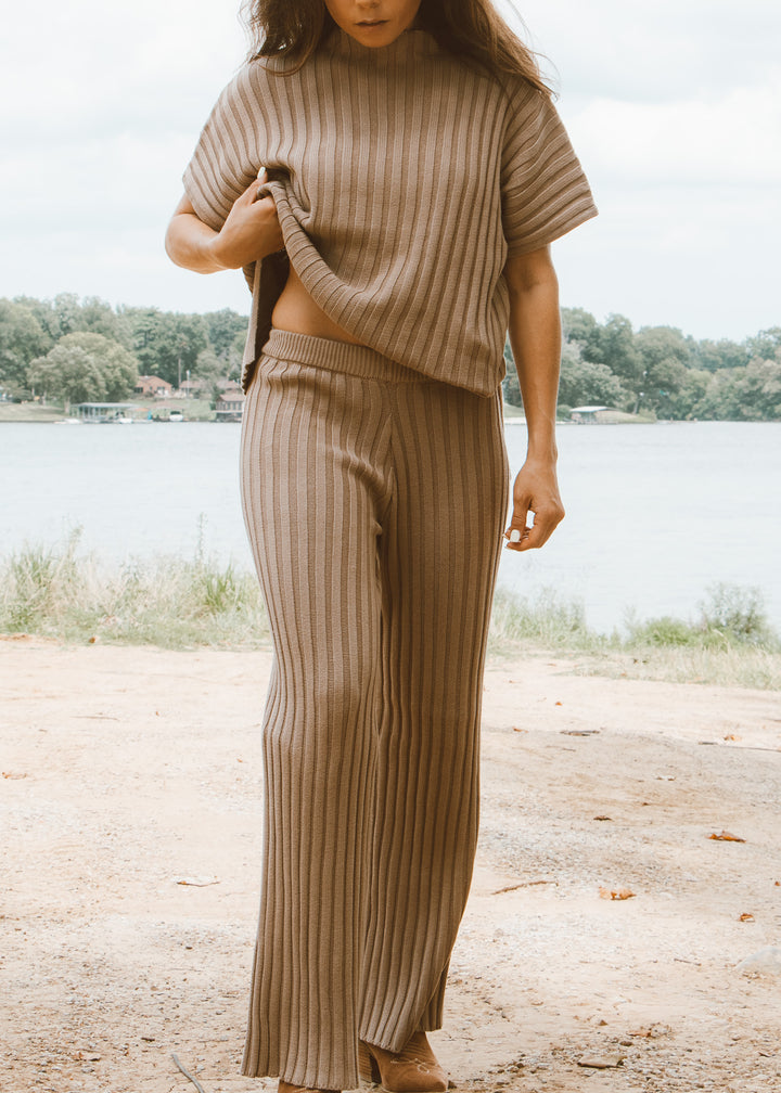 Person wearing a beige ribbed sweater and pants by a lake