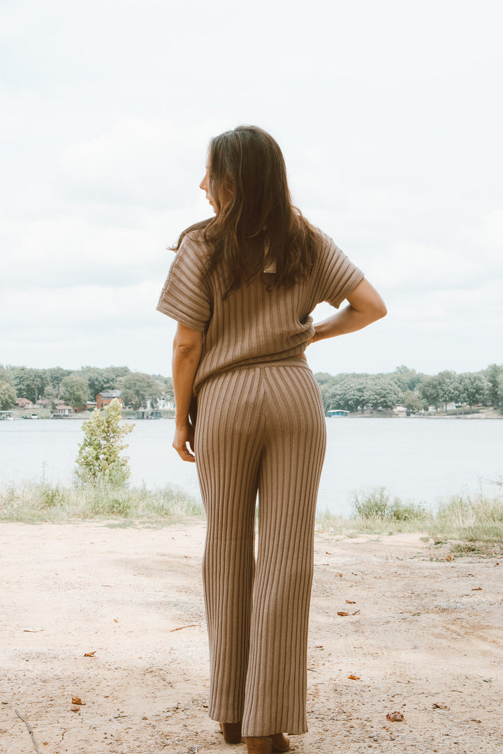 Woman in a beige ribbed outfit standing by a lake