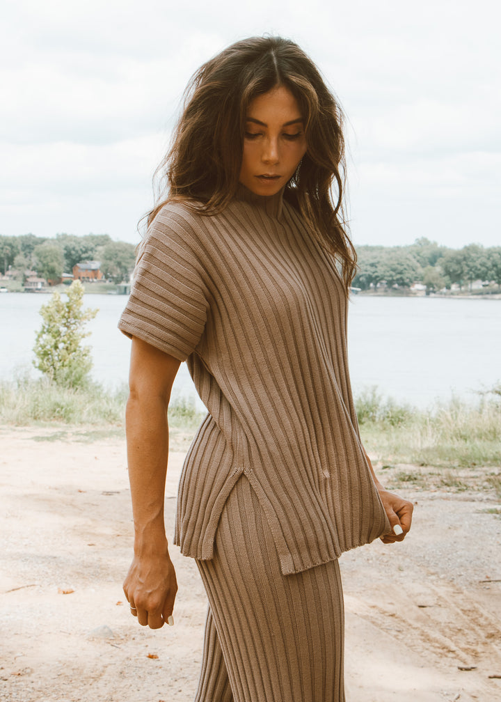 Woman wearing a beige ribbed outfit standing outdoors with a lake in the background