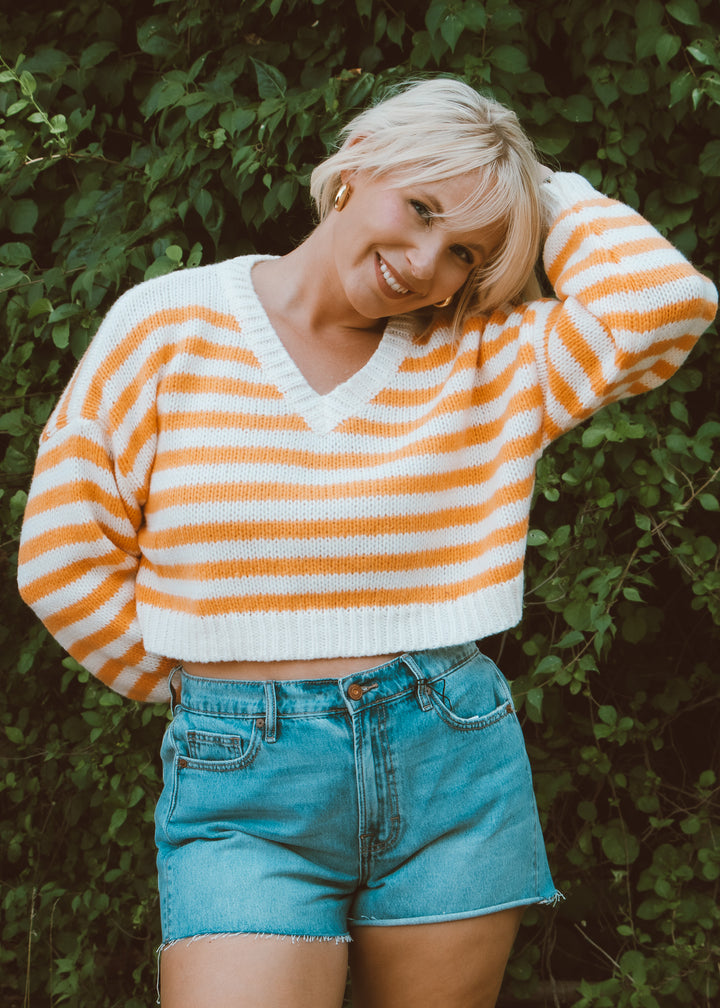 Woman wearing a striped sweater and denim shorts against a green leafy background
