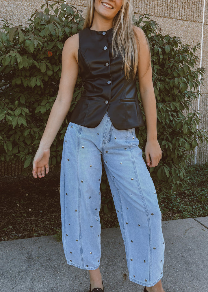 Woman wearing a black vest and light blue jeans standing outdoors.